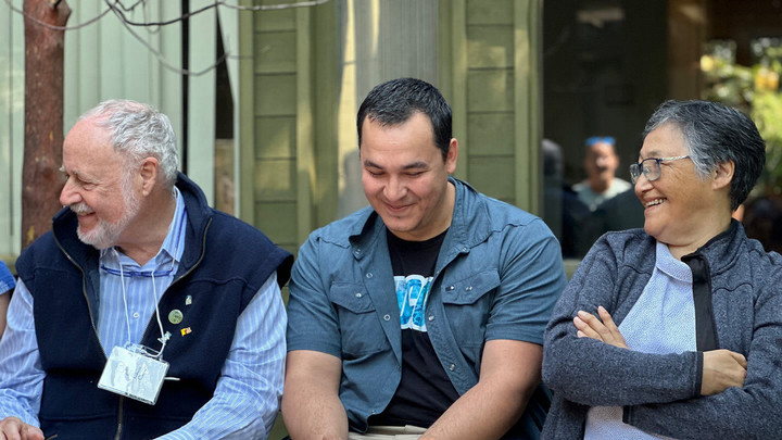 Three people sit together in a line, each smiling.